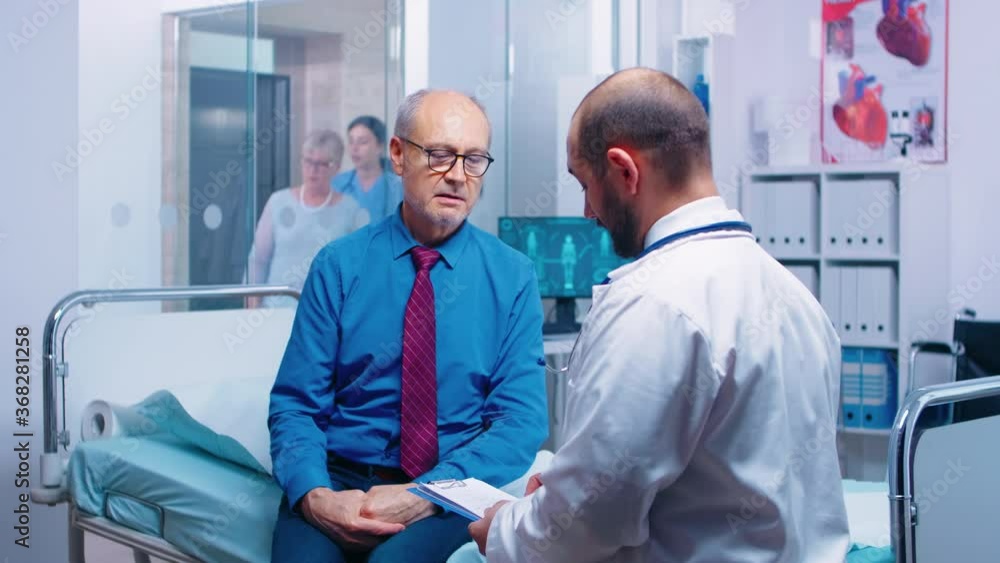 Senior man consulting with doctor sitting on hospital bed. Ill aged patient seeking medical advice for disease prevention from general practitioner in modern private clinic, doctor diagnosis Senior man consulting with doctor sitting on hospital bed. Ill aged patient seeking medical advice for disease prevention from general practitioner in modern private clinic, doctor diagnosis