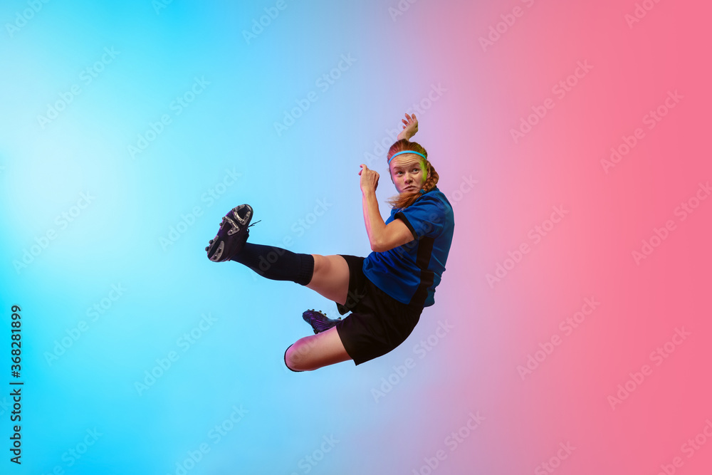 Obraz premium High jumping. Female soccer, football player training in action isolated on gradient studio background in neon light. Concept of motion, action, ahievements, healthy lifestyle. Youth culture.