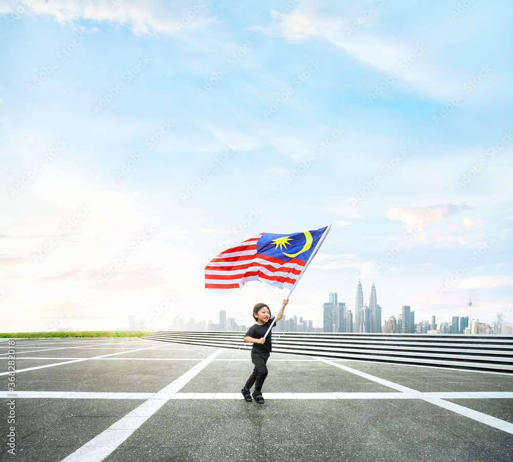 Fototapeta premium Happy boy running while holding Malaysia flag with cityscape.
