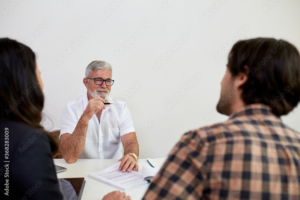 Three business people sitting at a desk, talking in a studio Three business people sitting at a desk, talking in a studio