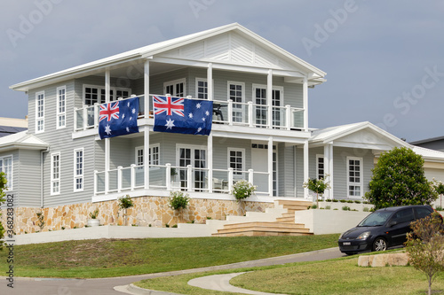 Grey and white Hamptons style house with two large Australian flags hanging from railings photo