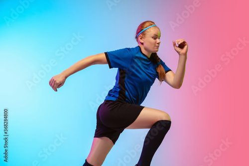 On the run. Female soccer, football player training in action isolated on gradient studio background in neon light. Concept of motion, action, ahievements, healthy lifestyle. Youth culture.