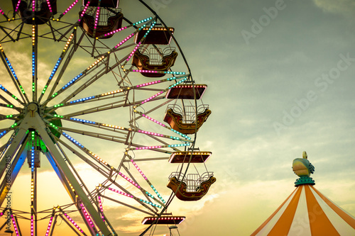Foto Colorful ferris wheel at sunset, illuminated by neon lights with a circus tent