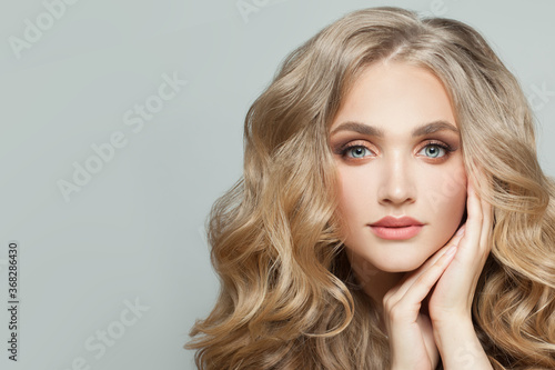 Cheerful young woman with healthy blonde wavy hair and clear skin on white