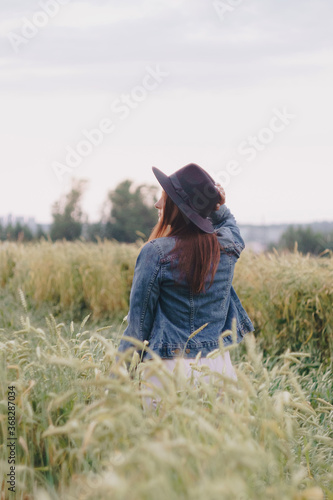 Beautiful young girl in a denim jacket in a green field of rye at sunset