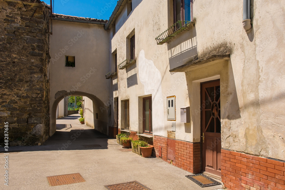 Obraz premium A lane in the centre of Podnanos, a village in the upper Vipava Valley in the Municipality of Vipava in the Primorska region of Slovenia. The bell tower of the parish church of Saint Vitus - known as