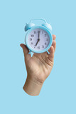 Female hand holding blue alarm clock on light blue background
