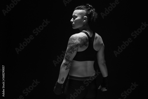 A young, female boxer with dark hair styled with a fade on one side, stands in contemplation of her next bout. 