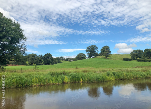 A photo of a canal in England with beautiful green fields and a blue sky 