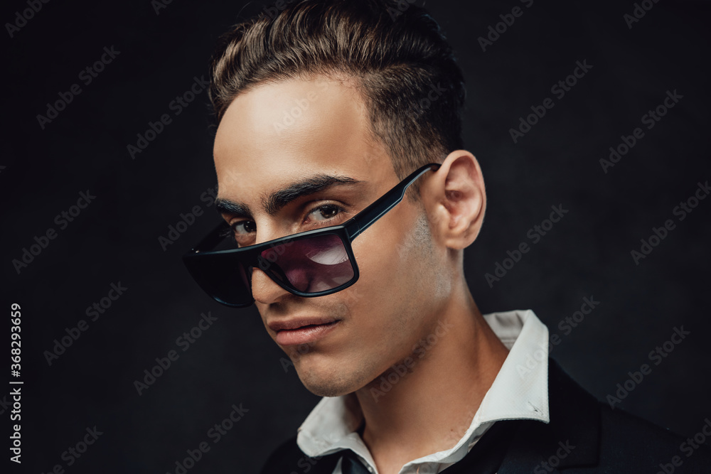 Handsome and successful. Close up portrait of a young businessman in black suit and sunglasses. Studio shot on a dark background