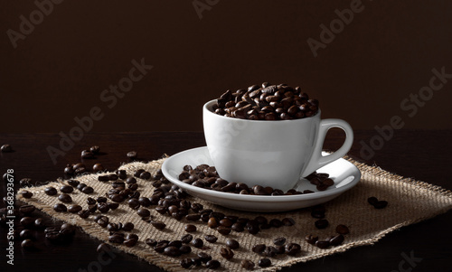 Roasted coffee beans in a white Cup on a wooden table. Coffee beans on burlap.
