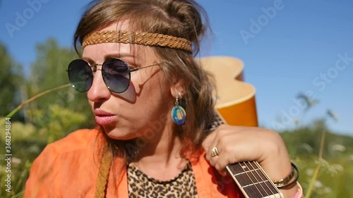 Slow motion. nature, summer vacation, vacation and people concept - happy smiling woman in sunglasses stands with a guitar on her shoulder. photo