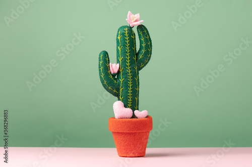 A toy felt blooming cactus with cute small hearts are on a light green background. Concept wedding proposal, gift, mother's day.
