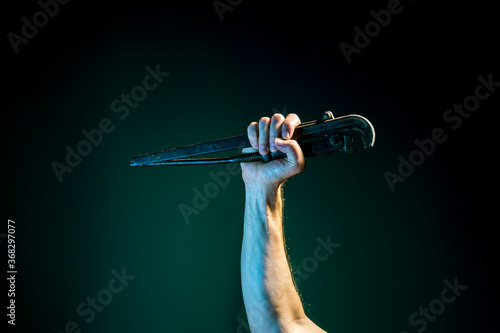 A raised Male hand holds a spanner on a dark  background