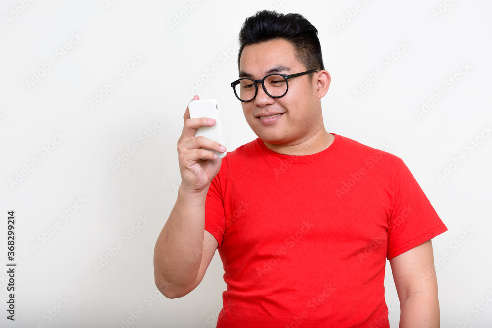 Portrait of happy young overweight Asian man using phone Portrait of happy young overweight Asian man using phone