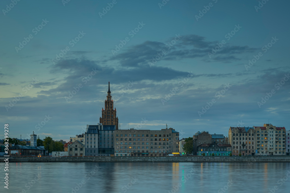 Night view on the illuminated riverside with reflection on the river in Riga
