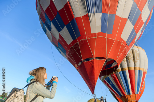 A girl with a large backpack and in a denim jacket takes a photo of a soaring air-balloon. photo