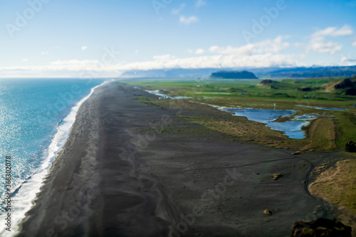 Iceland "Golden circle" journey. Top view from the cliff. Spring landscape - green volcanic meadows, 
desert coast of the Atlantic ocean, black sand beach, the spread river and clear blue sky