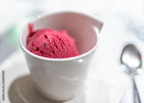 Close up of a decadent scoop of vivid pink sorbet served in a white bowl.