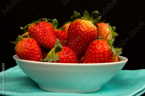 Red fresh strawberry in a bowl on black background.