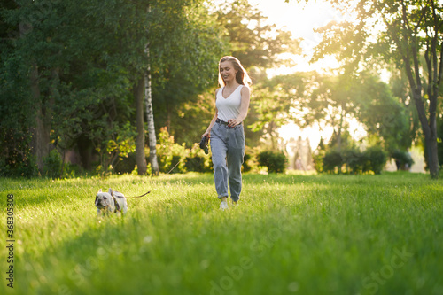 Young woman running with french bulldog in park.