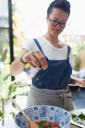 Woman sprinkling fresh herbs over bowl photo