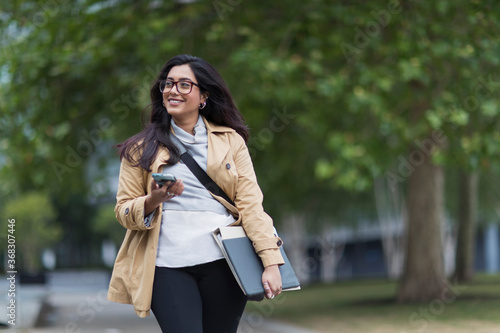 Smiling businesswoman walking with smart phone in park photo