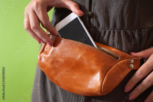 Fényképezés Hand puts phone to waist bag made from natural leather close-up view on the unre