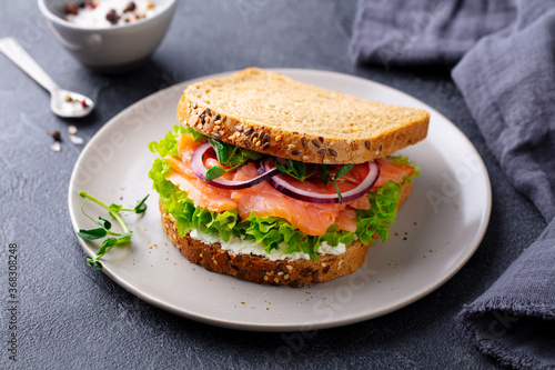 Sandwich with salmon, vegetables and cream cheese on plate. Grey background. Close up.