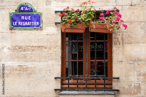 Canvas Print A window with shutters, bars and flower boxes is set into a stone wall on a street in Paris, France