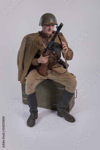 A male actor in the uniform of an officer and a helmet of the Soviet Army during the Second World War with a rifle in his hands sits on a military medical box photo