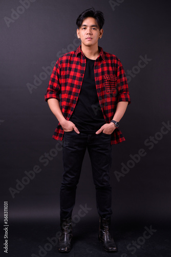 Young handsome Asian hipster man against black background
