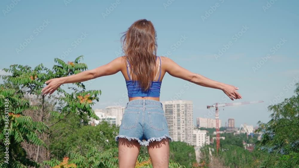 Sexy and Slim young woman in short denim shorts hands up on the background  city on a summer sunny day. Athletic Girl with a Perfect figure. Diet and  nutrition. Beautiful booty, close