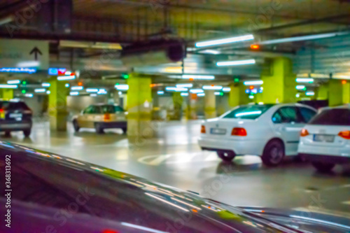 Parking lot cars blurred. Car lot parking space in underground city garage. Empty road asphalt background in soft focus. Industrial Shed or Parking Lot. © Maksym