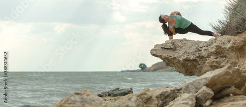 Yoga outdoors on a rocky beach. Young woman practicing yoga on a rocky seaside