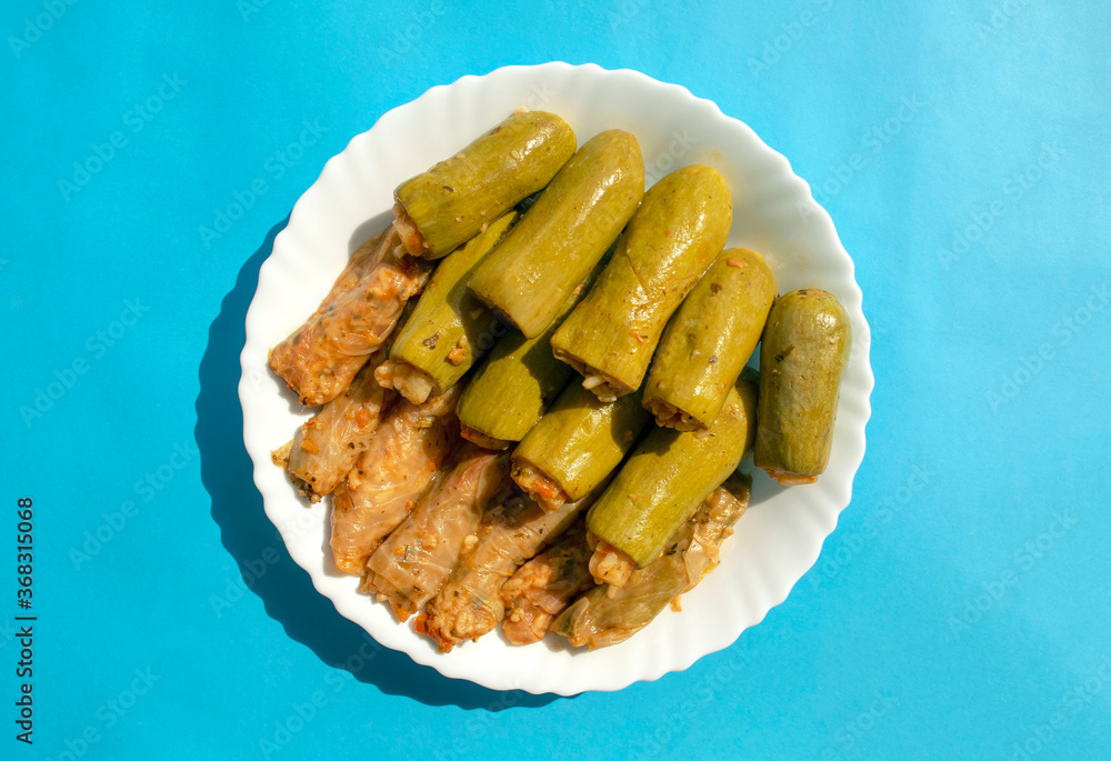 Traditional stuffed squash and cabbage rolls on white plate on blue