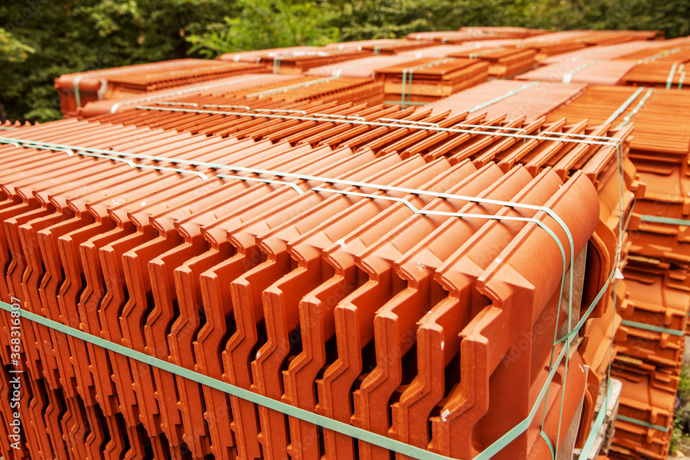 Red roof tiles are packed in standard packaging on building pallets for further transport.