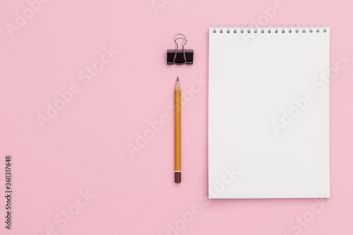 Lead pencil, binder and notepad with white sheets on a light pink background. Top view and copy space.