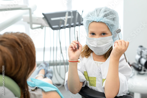 Caucasian girl playing at the dentist. Child holding dental instruments in hands, woman dentist depicts a patient