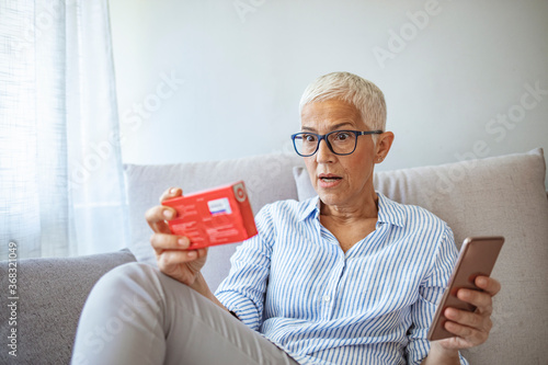 Фотография Senior woman talking on the phone and holding a pack of pills