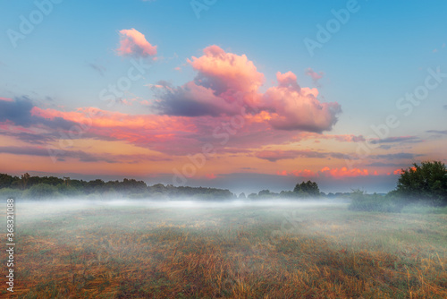 Landscape with foggy meadow and beautiful multicolored clouds during sunset