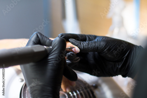 manicurist in black gloves is making manicure with a manicure drill apparatus