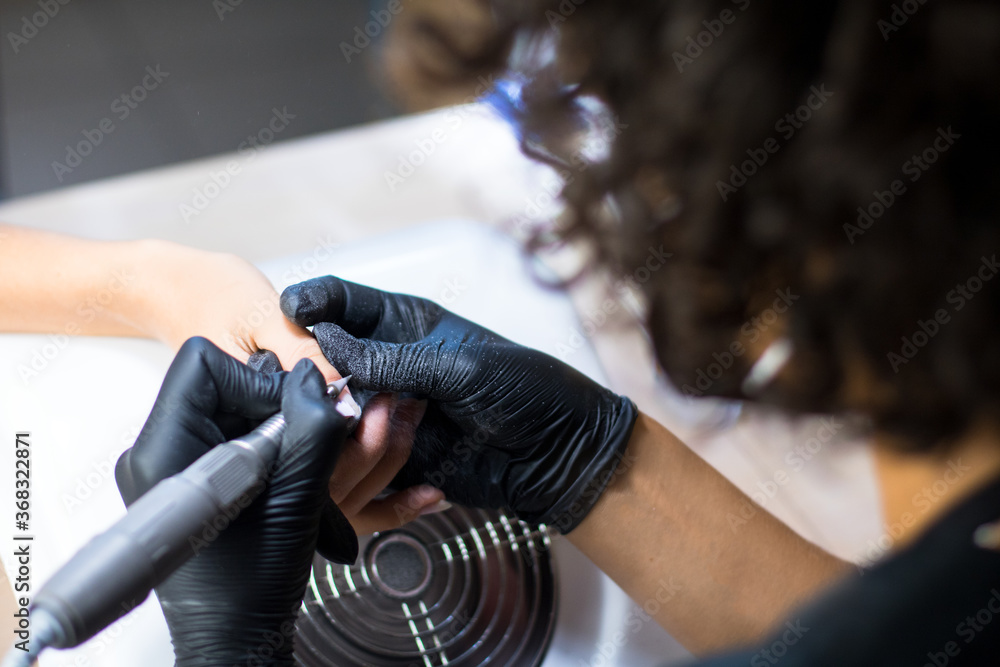manicurist in black gloves is making manicure with a manicure drill apparatus
