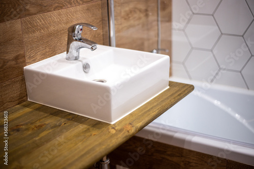 Bathroom design. Wall panels with wood texture. A square sink with a mixer sits on a shelf.