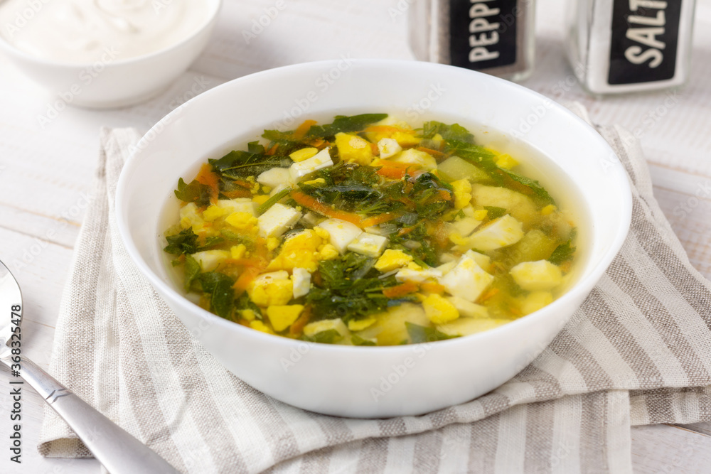 Nettle soup with eggs and sour cream on a white wooden table Nettle soup with eggs and sour cream on a white wooden table