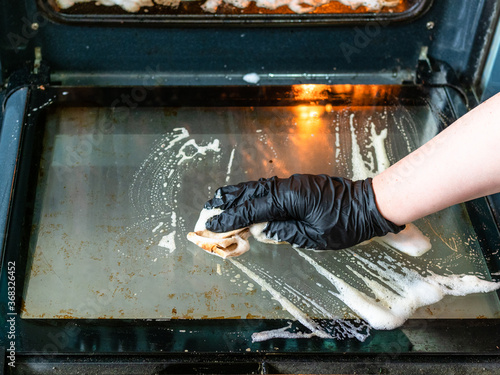 Fotografi cleaning oven in home kitchen - female hand cleans glass door of dirty oven with