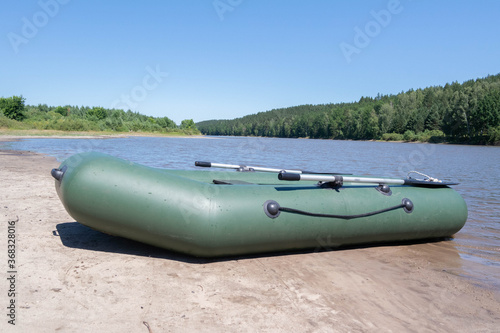 An inflatable rubber boat stands on the banks of a river or lake surrounded by forest. Sunny daytime summer landscape. Background for river walks on water or a concept for fishing. Alone with nature.