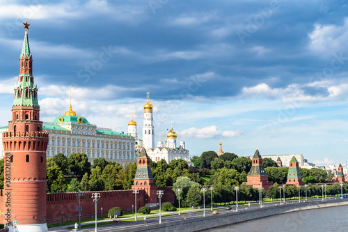 view of Kremlin with embankment of Moskva River under dark blue rainy clouds during city sightseeing tour on excursion bus in Moscow city on sunny summer day