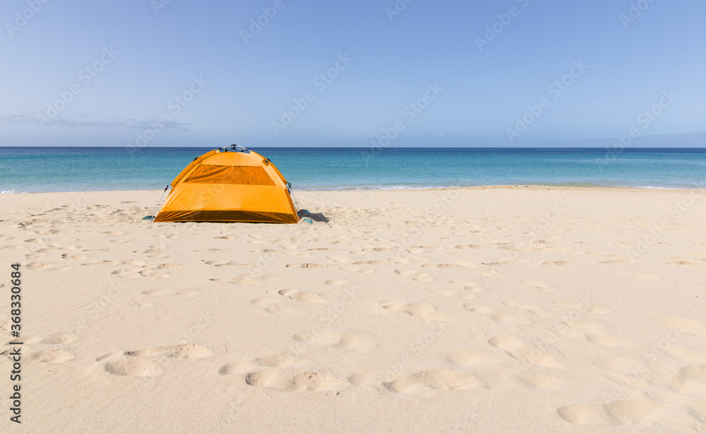 An orange tent set up on the beach very close to the turquoise water of the beaches on the island of Fuerteventura. Nomadic spirit. An orange tent set up on the beach very close to the turquoise water of the beaches on the island of Fuerteventura. Nomadic spirit.