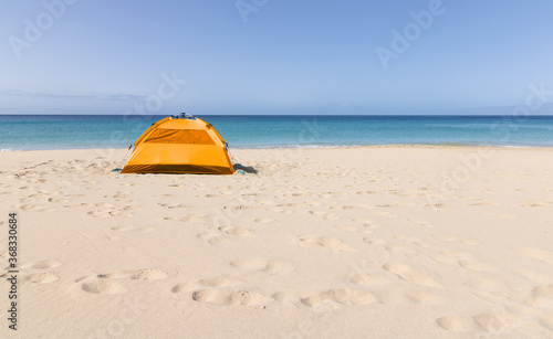 An orange tent set up on the beach very close to the turquoise water of the beaches on the island of Fuerteventura. Nomadic spirit.